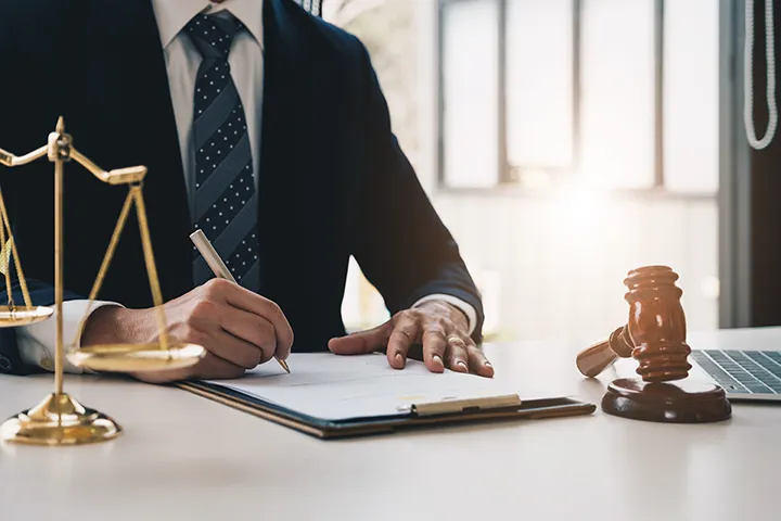 Hombre de traje escribiendo en la carpeta con la balanza de la justicia, el mazo y el portátil sobre el escritorio