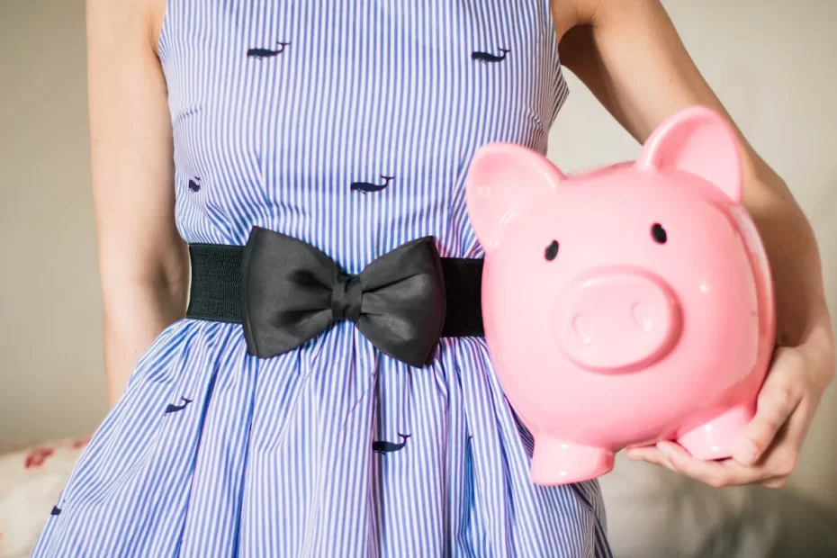 Close-up of a woman in a striped dress holding a pink piggy bank, symbolizing savings and financial planning.